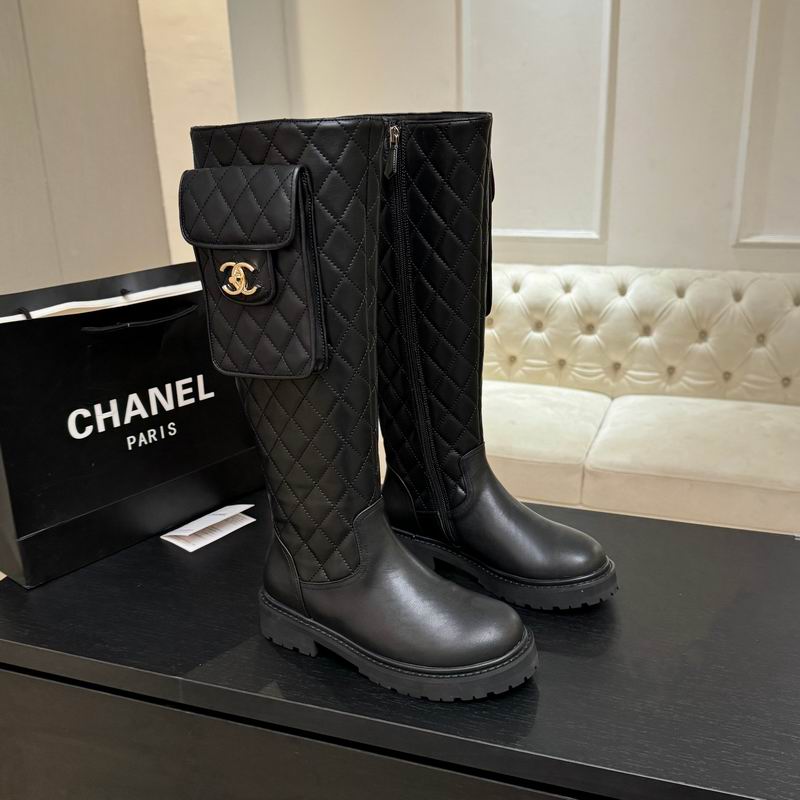 Chanel black quilted leather knee-high boots with gold CC logo pocket and chunky lug sole, displayed with Chanel shopping bag